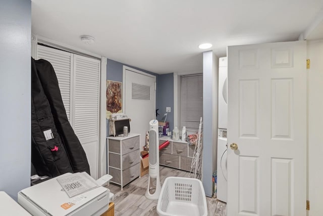 bedroom with light wood-type flooring, two closets, and stacked washer and dryer