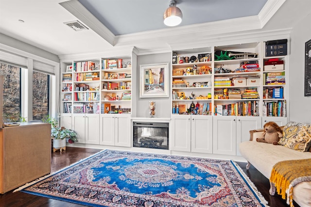 living area featuring wood finished floors, visible vents, built in features, and ornamental molding