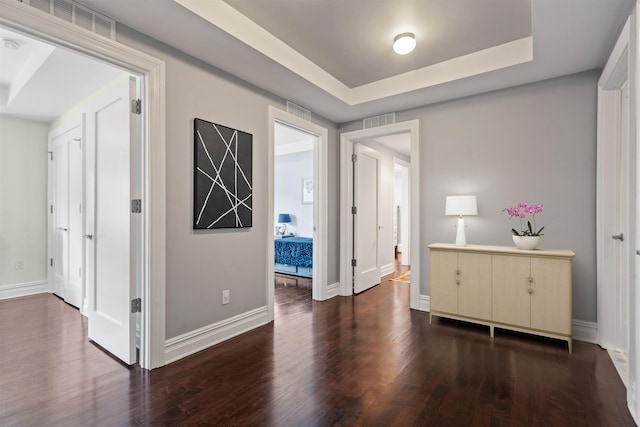 hallway featuring a tray ceiling, baseboards, visible vents, and dark wood-style flooring
