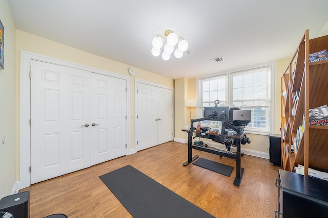 workout room featuring visible vents, baseboards, an inviting chandelier, and wood finished floors