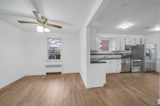 kitchen featuring sink, light wood-type flooring, appliances with stainless steel finishes, radiator heating unit, and white cabinets