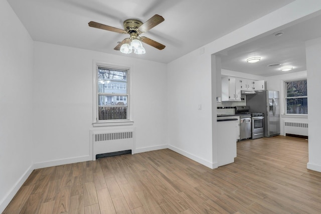 kitchen with radiator heating unit, stainless steel appliances, light hardwood / wood-style floors, and white cabinets