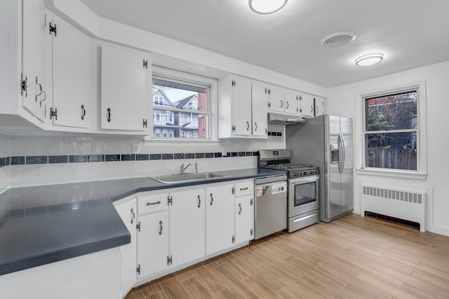 kitchen with sink, tasteful backsplash, radiator heating unit, stainless steel appliances, and white cabinets