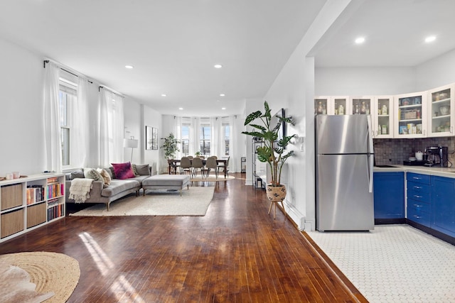 kitchen featuring wood finished floors, blue cabinetry, freestanding refrigerator, tasteful backsplash, and glass insert cabinets