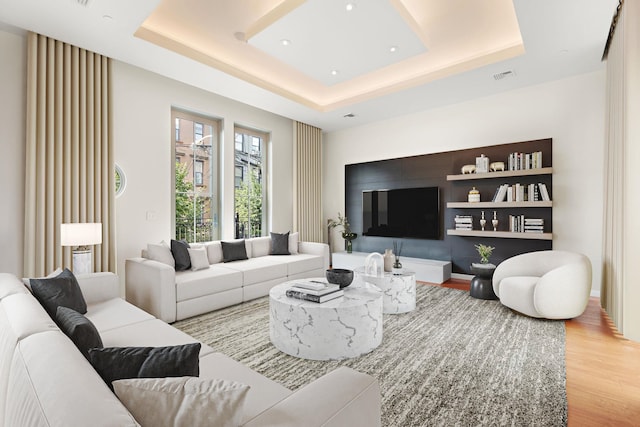 living room with light hardwood / wood-style floors and a raised ceiling