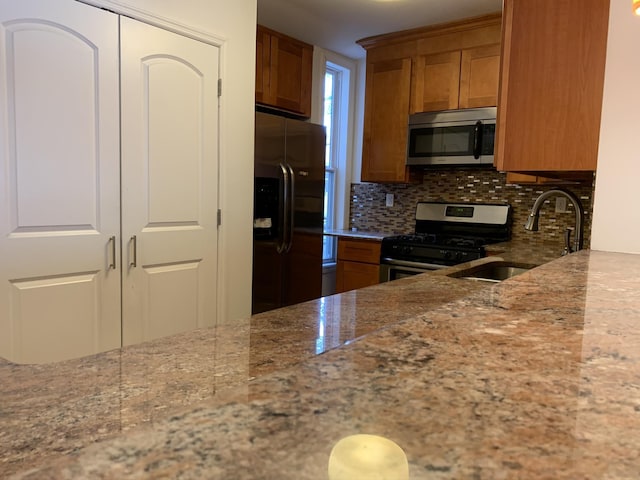612 Palisade Ave, Jersey City, NJ 07307 - kitchen featuring backsplash, light stone countertops, brown cabinetry, stainless steel appliances, and a sink
