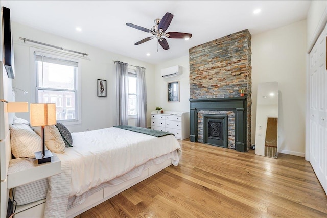 bedroom with ceiling fan, a stone fireplace, a wall mounted air conditioner, light hardwood / wood-style floors, and a closet