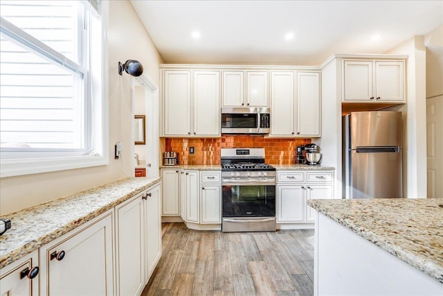 kitchen featuring appliances with stainless steel finishes, backsplash, light wood-type flooring, white cabinetry, and light stone countertops