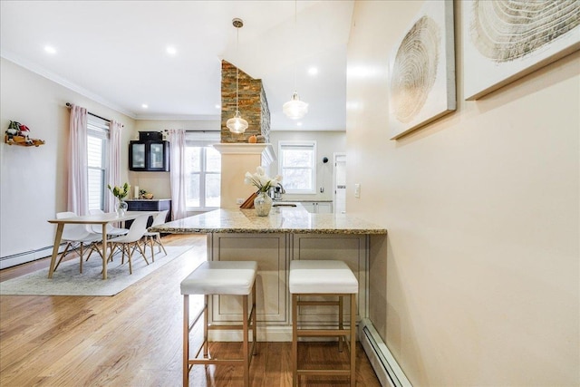 kitchen with light stone countertops, hanging light fixtures, light wood-type flooring, ornamental molding, and a breakfast bar