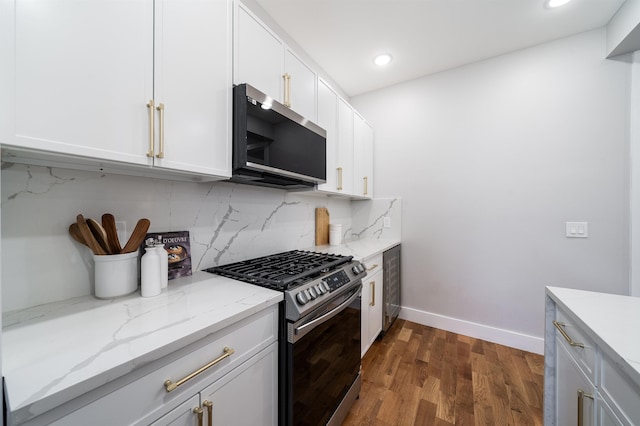 kitchen featuring appliances with stainless steel finishes, white cabinetry, backsplash, light stone countertops, and dark hardwood / wood-style flooring