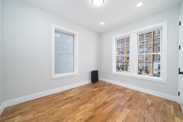 empty room featuring hardwood / wood-style flooring, radiator heating unit, and a healthy amount of sunlight