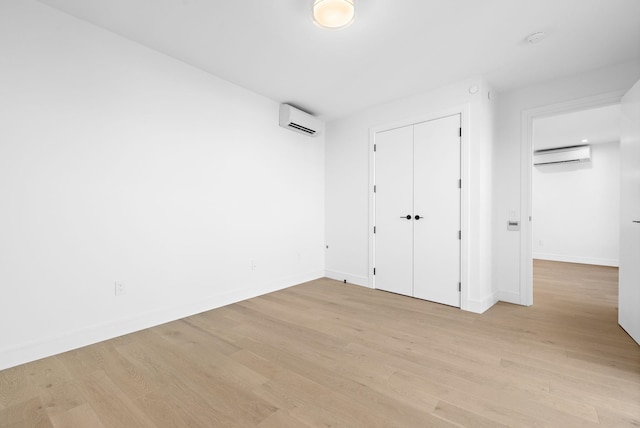 unfurnished bedroom with a closet, an AC wall unit, light wood-style flooring, and baseboards