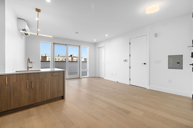 kitchen with brown cabinets, light wood-style flooring, electric panel, a sink, and a wall mounted air conditioner