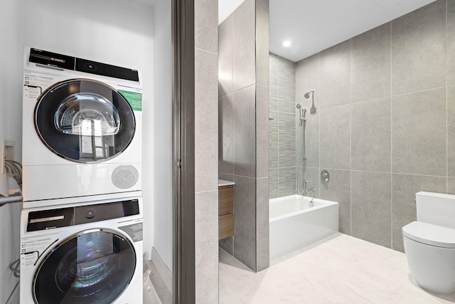 bathroom featuring toilet, bathtub / shower combination, tile walls, and stacked washer / dryer