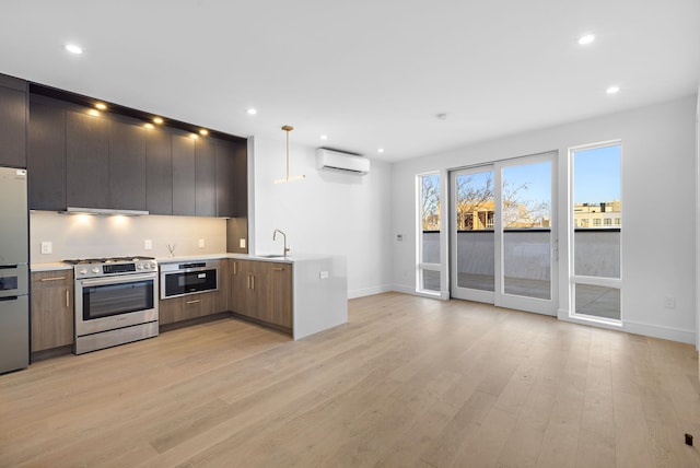 kitchen featuring light countertops, appliances with stainless steel finishes, a wall mounted AC, light wood finished floors, and modern cabinets