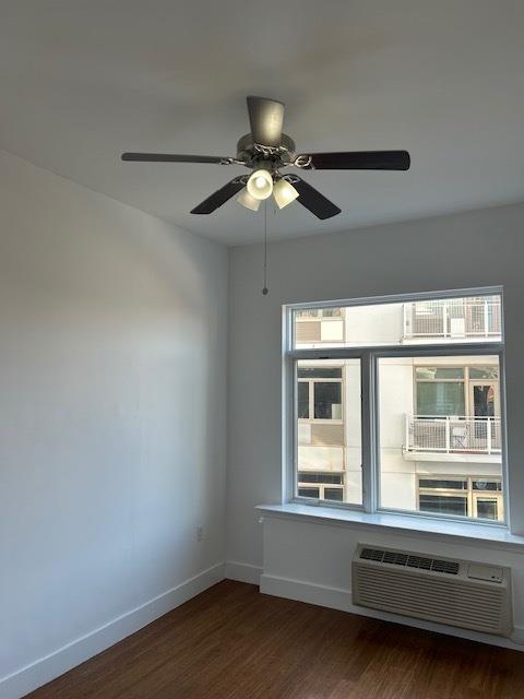 unfurnished room with ceiling fan, an AC wall unit, and dark hardwood / wood-style floors