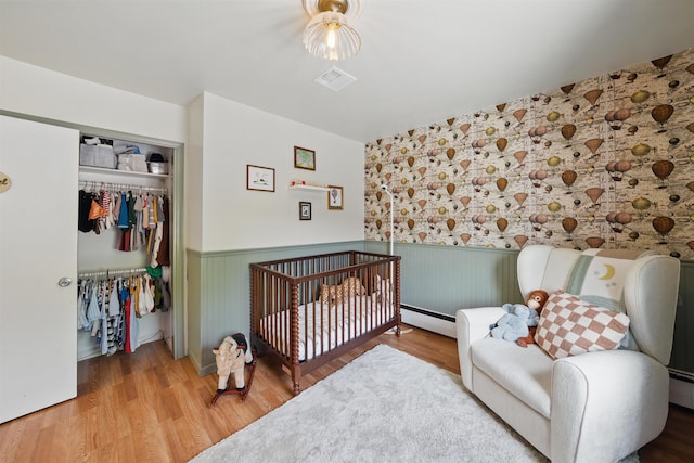 bedroom featuring baseboard heating, a wainscoted wall, visible vents, and a closet
