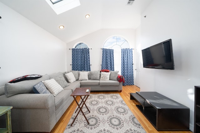 living room with a skylight, high vaulted ceiling, and light wood-type flooring