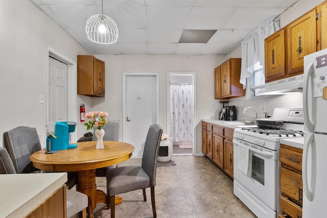kitchen featuring a drop ceiling, a sink, brown cabinetry, white appliances, and under cabinet range hood