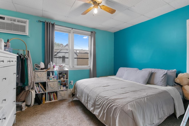 carpeted bedroom with a wall mounted air conditioner, a ceiling fan, and a drop ceiling