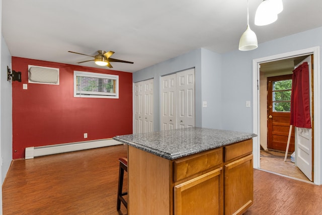 kitchen with wood finished floors, decorative light fixtures, a kitchen bar, a ceiling fan, and baseboard heating