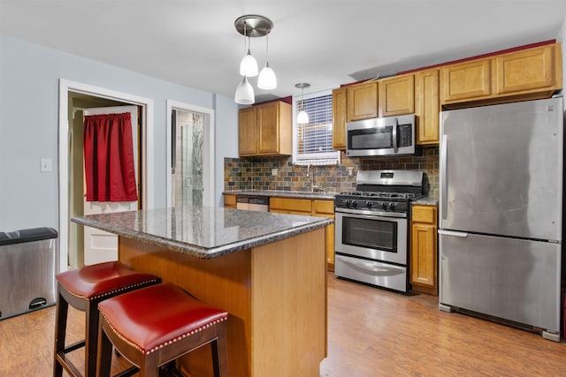 kitchen featuring backsplash, light wood-style floors, appliances with stainless steel finishes, and a kitchen bar