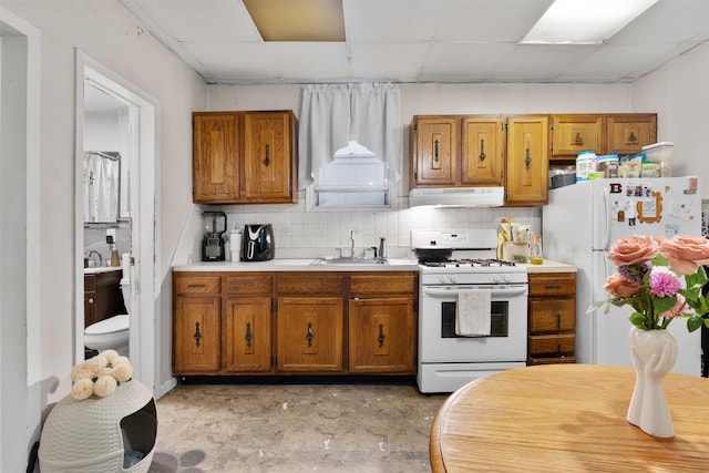 kitchen with brown cabinetry, white appliances, range hood, and a drop ceiling