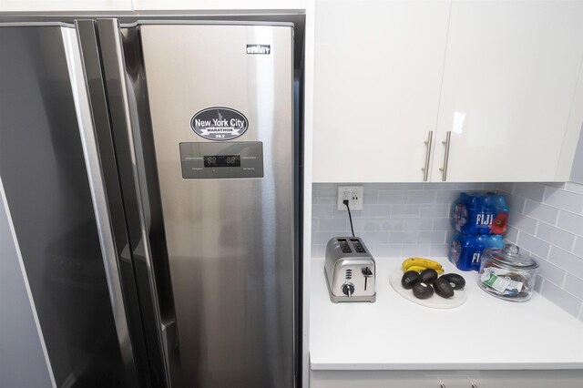 kitchen view of freestanding refrigerator, white cabinets, tasteful backsplash, and light countertops