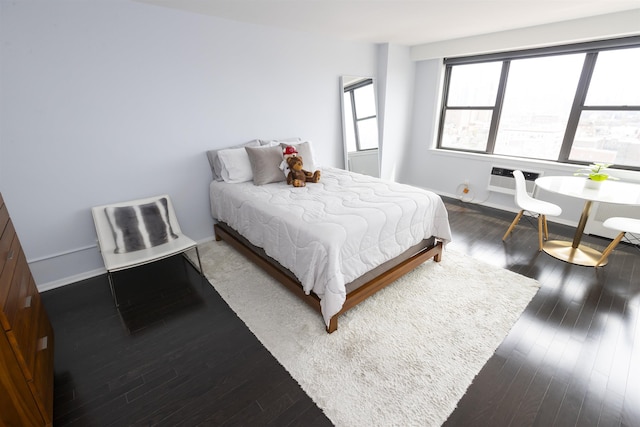 bedroom featuring wood finished floors, baseboards, and a wall mounted AC