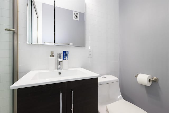 bathroom featuring toilet, tile walls, and vanity