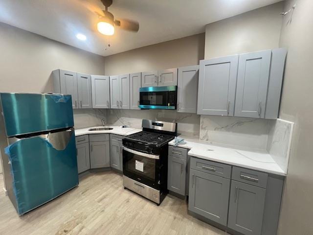 kitchen featuring light wood-style flooring, gray cabinets, a sink, tasteful backsplash, and stainless steel appliances