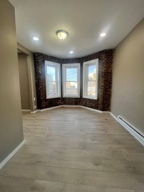 spare room with brick wall, baseboards, recessed lighting, light wood-style flooring, and a baseboard radiator