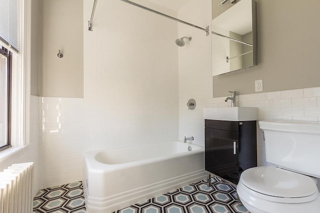 full bathroom with vanity, radiator, tiled shower / bath, toilet, and tile walls