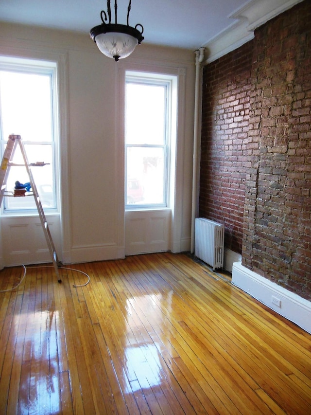 unfurnished room featuring radiator heating unit, light hardwood / wood-style floors, and brick wall