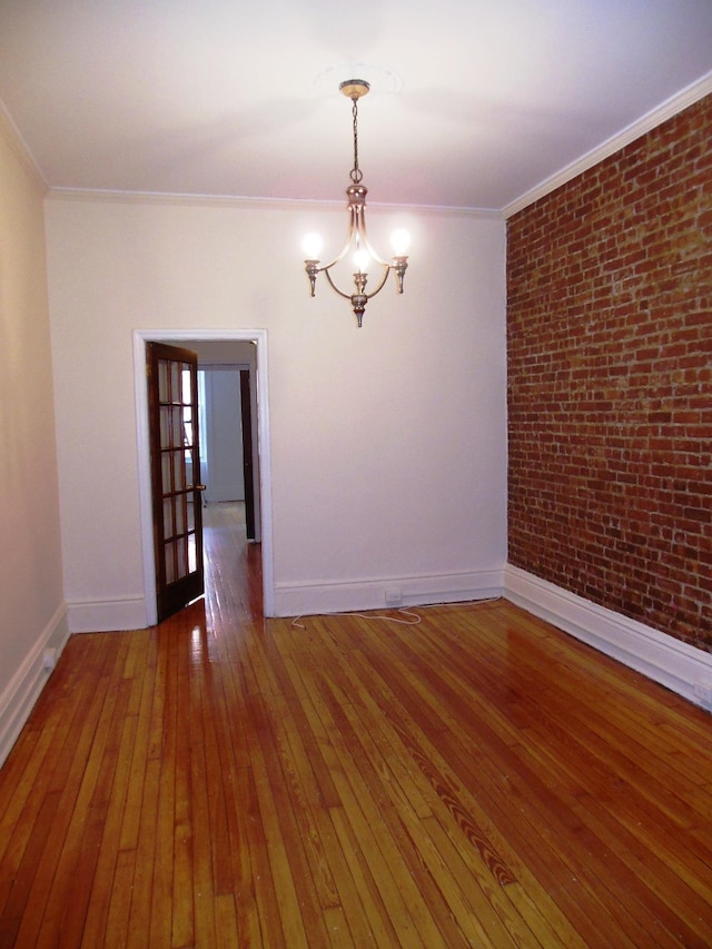 spare room with hardwood / wood-style flooring, a notable chandelier, crown molding, and brick wall