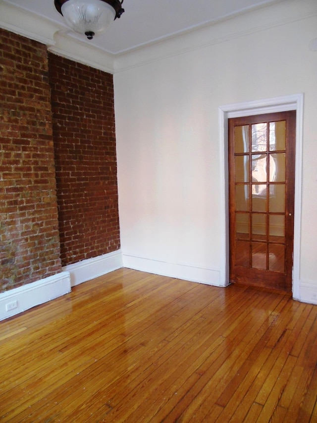 unfurnished room featuring hardwood / wood-style floors, crown molding, and brick wall