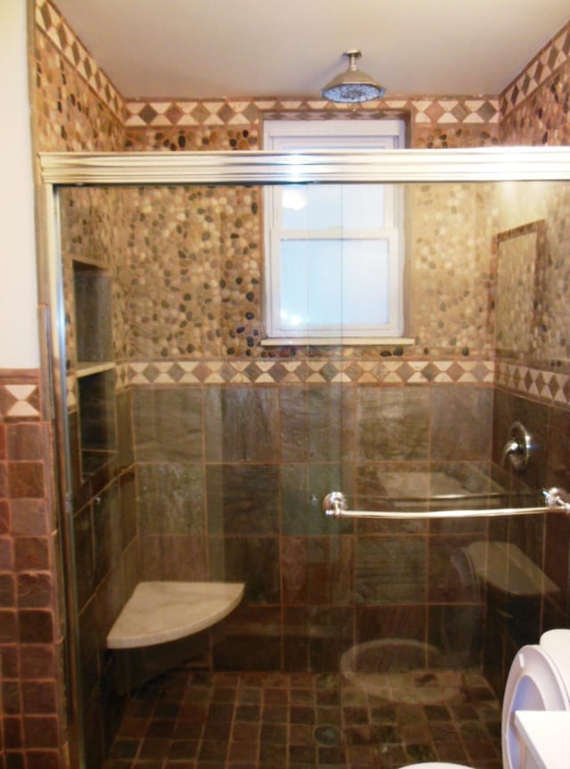 bathroom featuring a shower with door and toilet