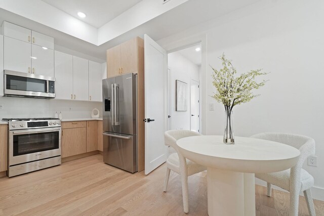 kitchen featuring white cabinets, light wood-type flooring, light brown cabinetry, and appliances with stainless steel finishes