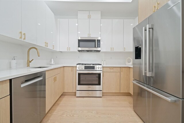 kitchen with stainless steel appliances, light brown cabinets, white cabinets, and light hardwood / wood-style flooring