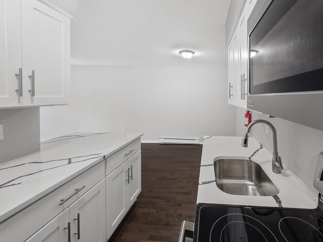 kitchen with a sink, white cabinetry, baseboard heating, light stone countertops, and dark wood finished floors