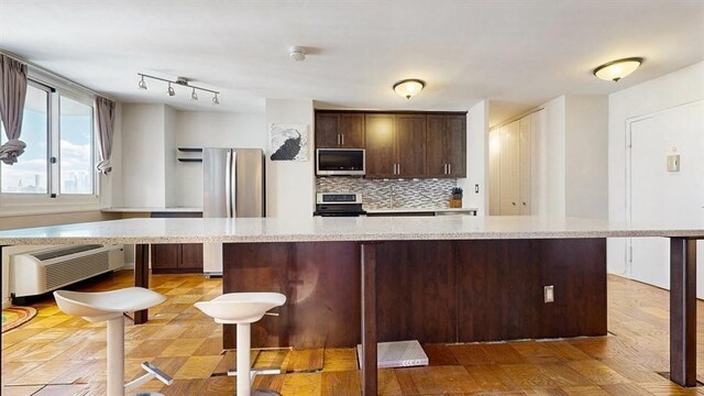 100 Manhattan Ave Unit 1912, Union City, NJ 07087 - kitchen with backsplash, a kitchen island, dark brown cabinetry, a wall unit AC, and appliances with stainless steel finishes