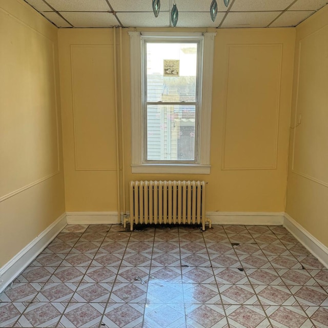 unfurnished room featuring radiator, a paneled ceiling, and light tile patterned flooring