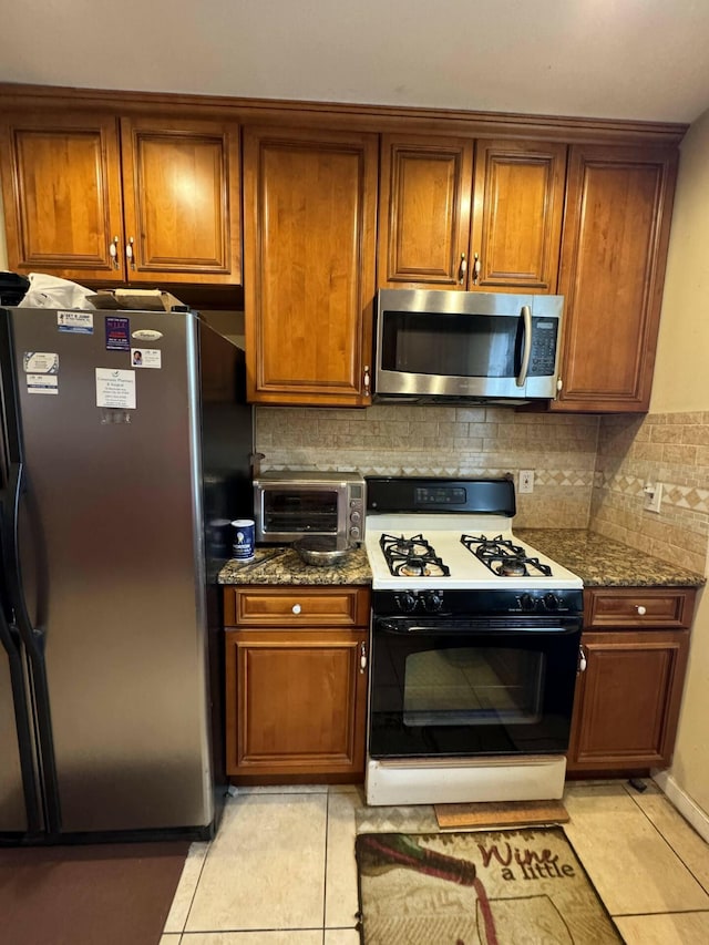 kitchen featuring dark stone countertops, decorative backsplash, light tile patterned flooring, and stainless steel appliances