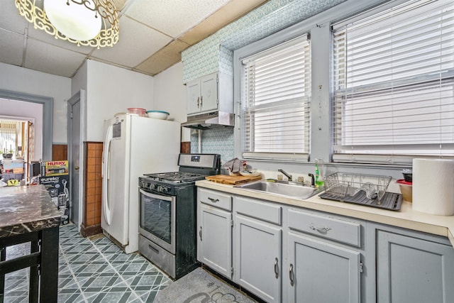 kitchen with a paneled ceiling, white fridge with ice dispenser, gray cabinets, stainless steel range with gas stovetop, and sink