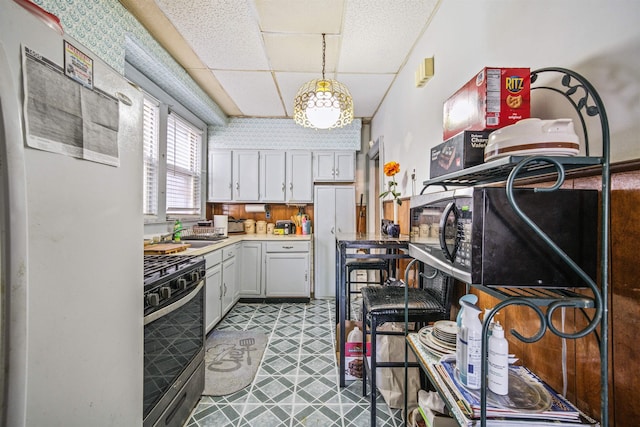 kitchen with stainless steel range with gas stovetop, pendant lighting, refrigerator, sink, and white cabinetry