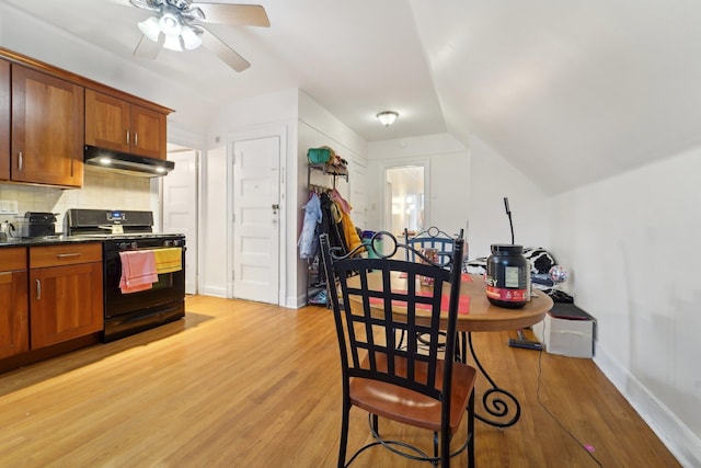 kitchen with lofted ceiling, dark countertops, under cabinet range hood, backsplash, and gas stove