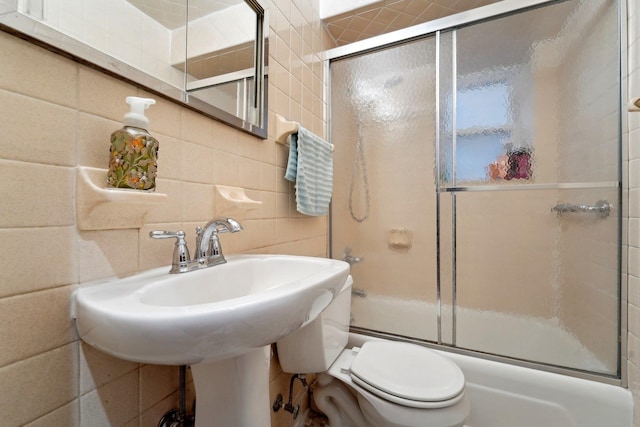 full bath with tile walls, toilet, and shower / bath combination with glass door