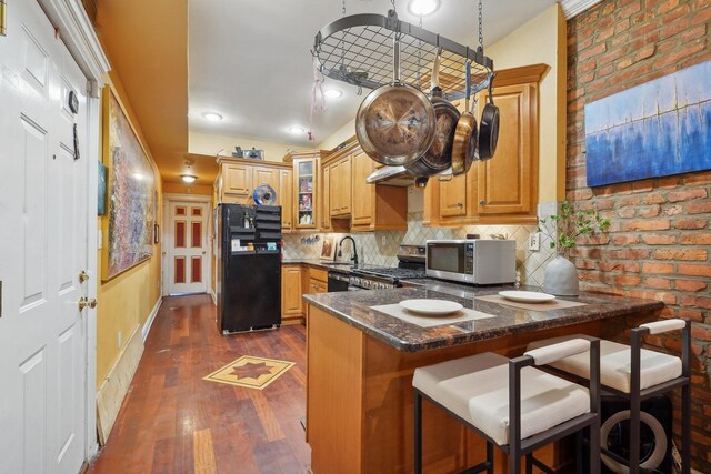 kitchen featuring black fridge, a kitchen bar, tasteful backsplash, kitchen peninsula, and dark stone counters