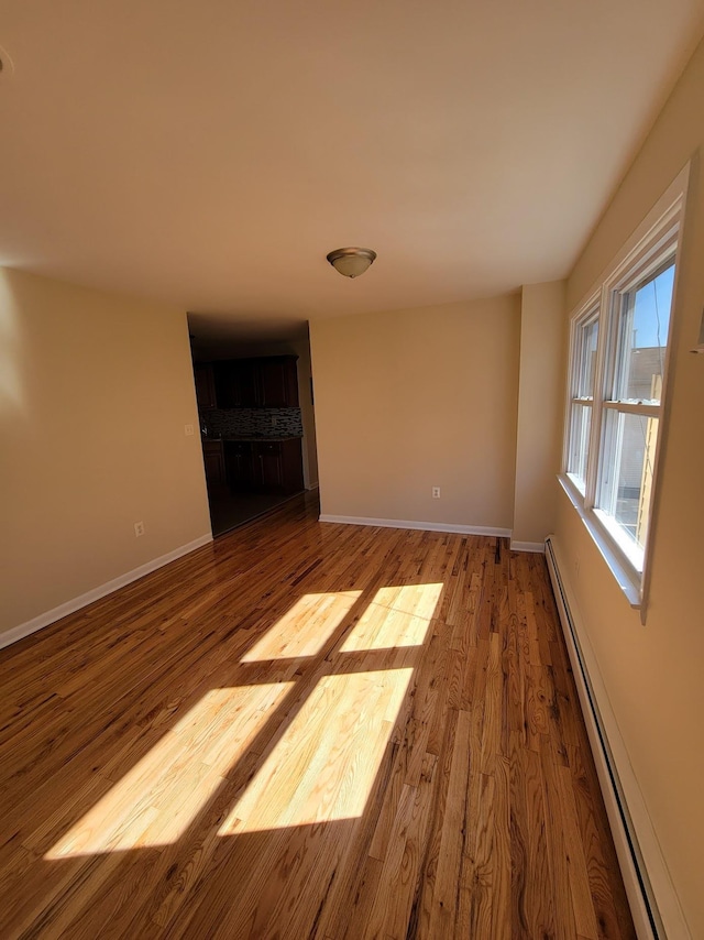 empty room featuring a baseboard heating unit, baseboards, and wood finished floors