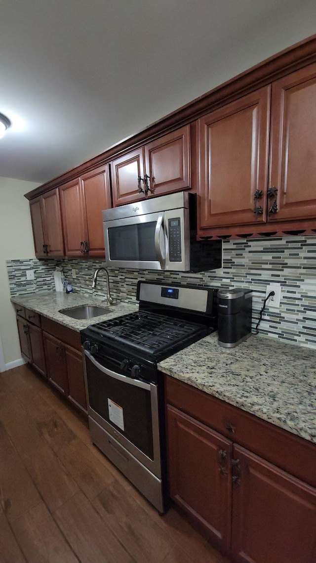 kitchen featuring a sink, tasteful backsplash, stainless steel appliances, light stone countertops, and dark wood-style flooring